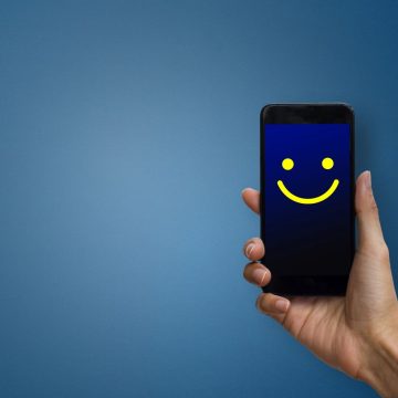 Cliente feliz Conceptual the customer responded to the digital survey. The client showing mobile phone screen with happy face. Depicts that customer is very satisfied. Service experience and satisfaction concept.